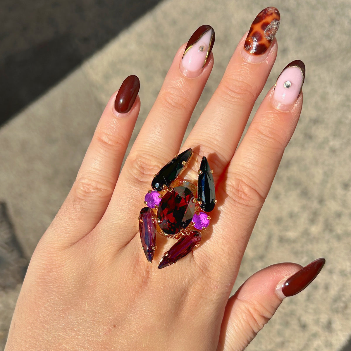 Bague réglable Lumen Mûre Crézus avec grand cristal ovale grenat, cristaux noirs et prune allongés, deux cristaux ronds violet orchidée et monture dorée texturée.