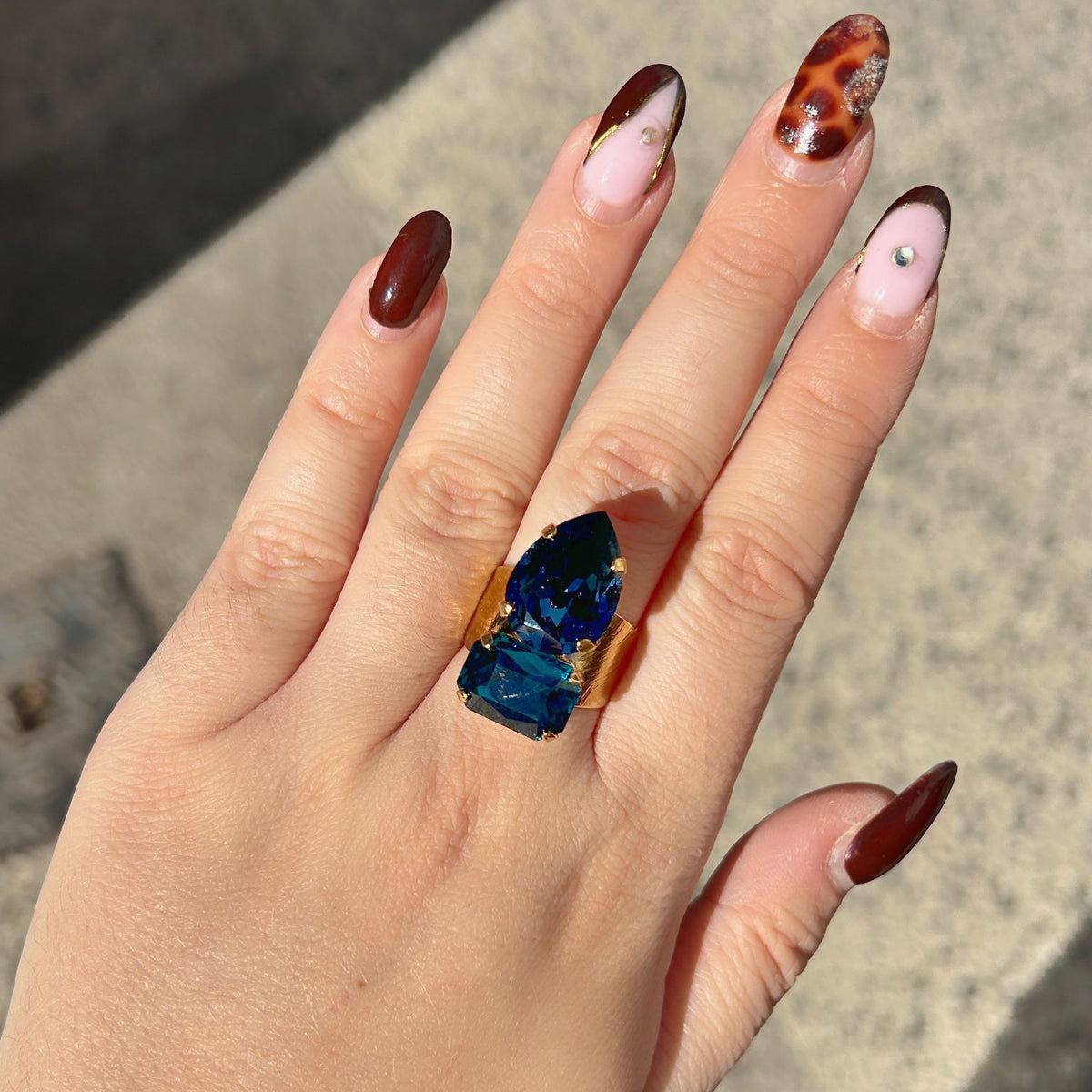 Bague Lyra Azur Crézus avec deux cristaux facettés bleu saphir et bleu pétrole, en forme de goutte et de rectangle, sur une large monture dorée texturée – Divinity Sète.