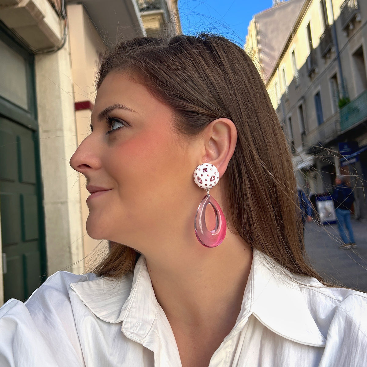 Boucles d'oreilles à clips Céleste Rose Francine Bramli Paris, attaches rondes blanches ornées de strass roses et pendentifs gouttes ajourées en résine rose translucide – Divinity Sète.