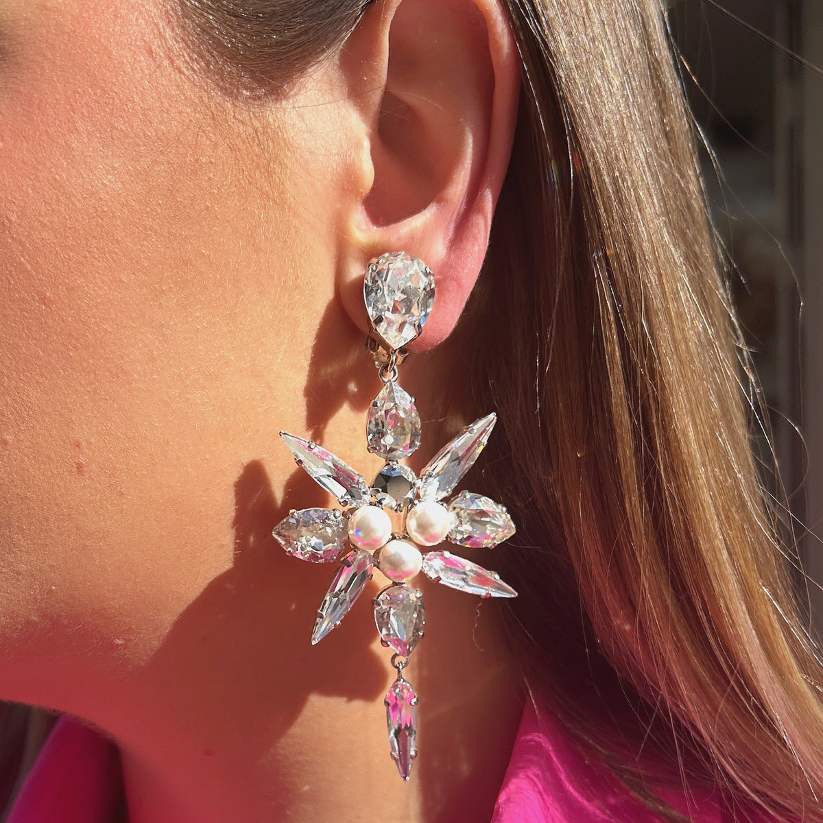 Boucles d'oreilles Celyna Silver à clips Crézus, modèle floral argenté composé de cristaux transparents facettés en forme de goutte et de navette, de trois perles blanches centrales et d'une pampille en cristal suspendue.