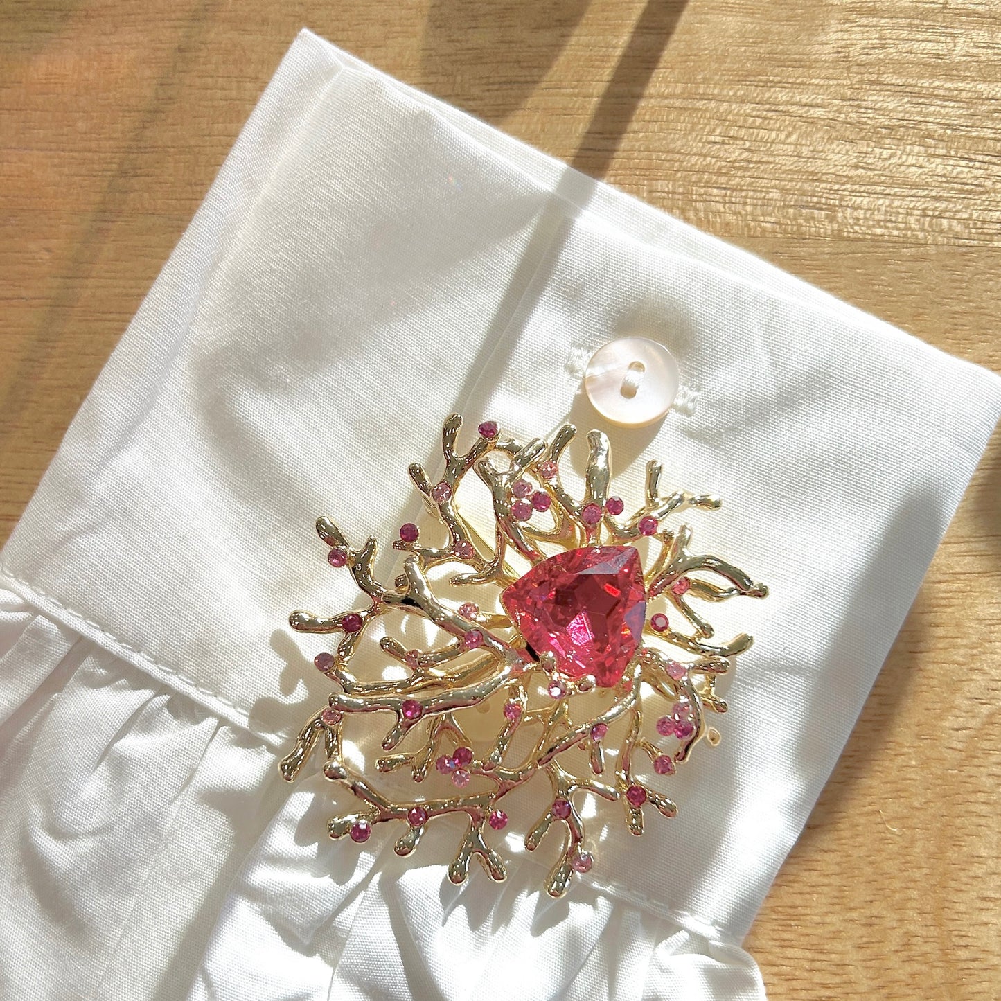 Détail de la broche corail dorée avec strass roses