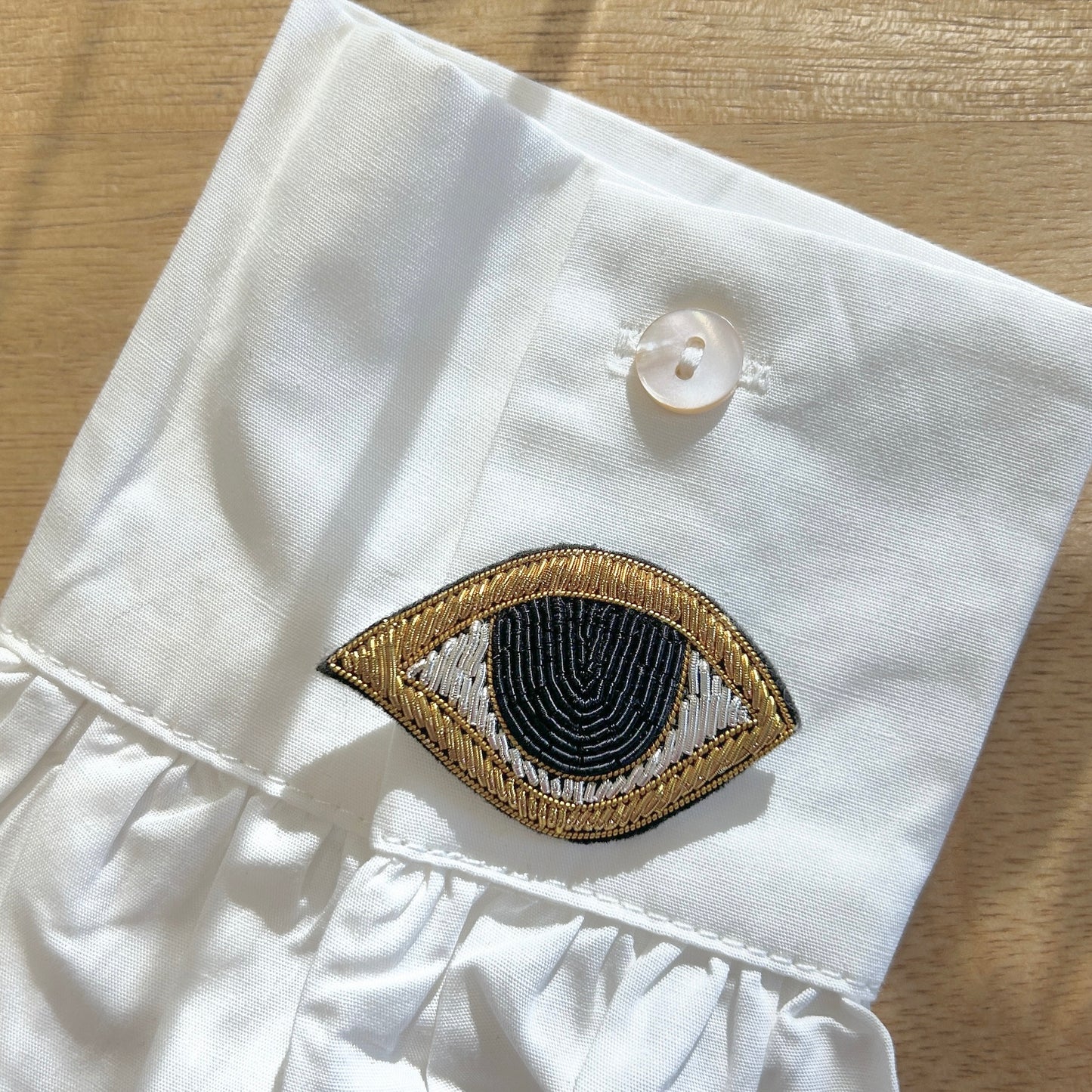 Détail broderie broche œil noir doré