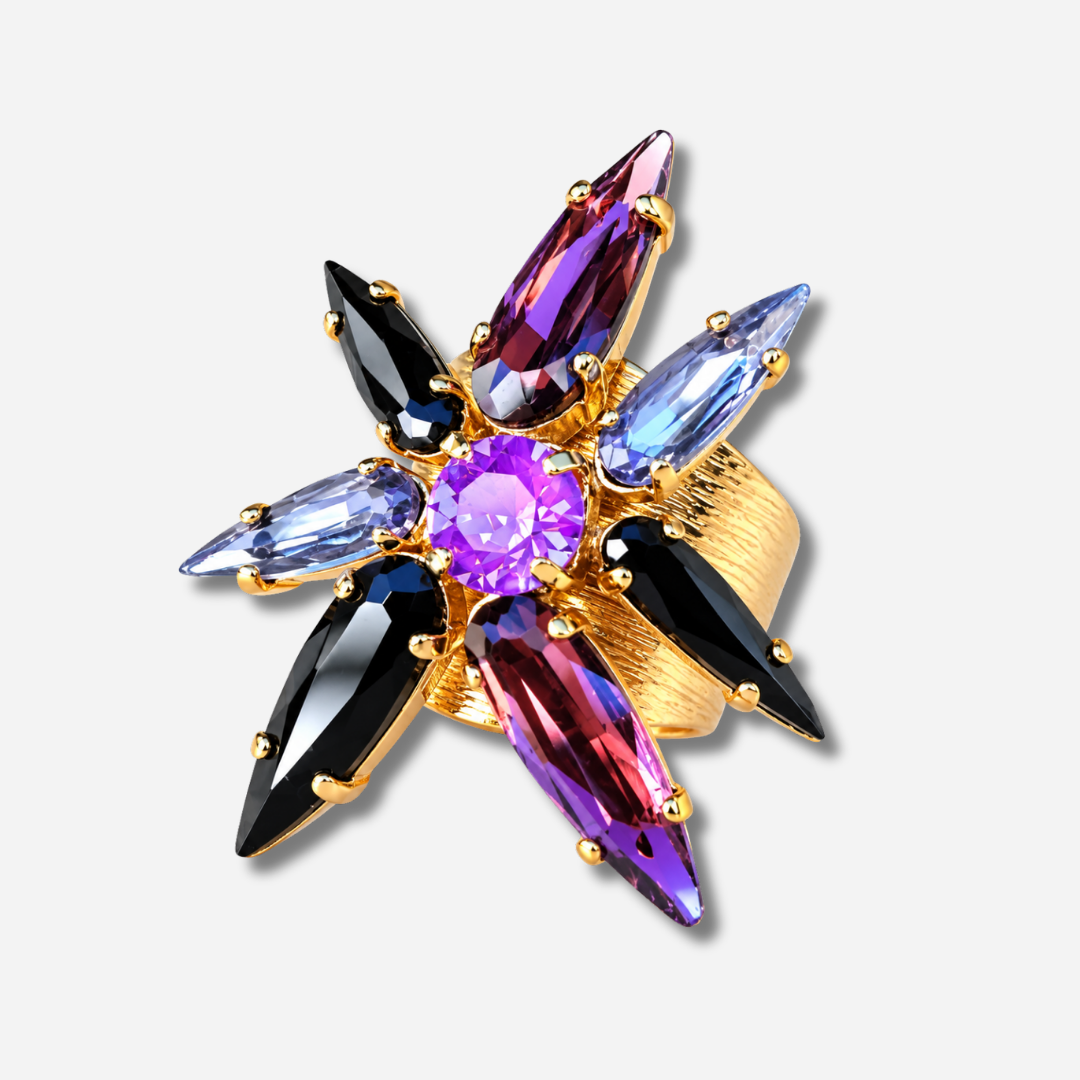 Bague Astra Mûre Crézus en forme d'étoile avec cristal central rond violet orchidée, huit cristaux pointus noirs, prune et bleu lavande sur large monture dorée texturée.