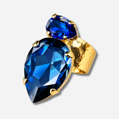 Bague Calypso Azur Crézus avec grand cristal bleu nuit en forme de goutte, petit cristal bleu saphir et monture dorée martelée – Divinity Sète.