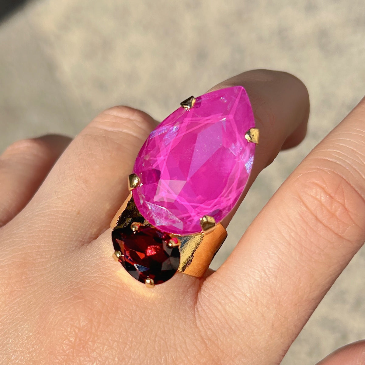 Bague Calypso Mûre Crézus avec grand cristal rose fuchsia en forme de goutte, petit cristal facetté couleur mûre et grenat, sertissage doré à griffes et anneau large martelé.