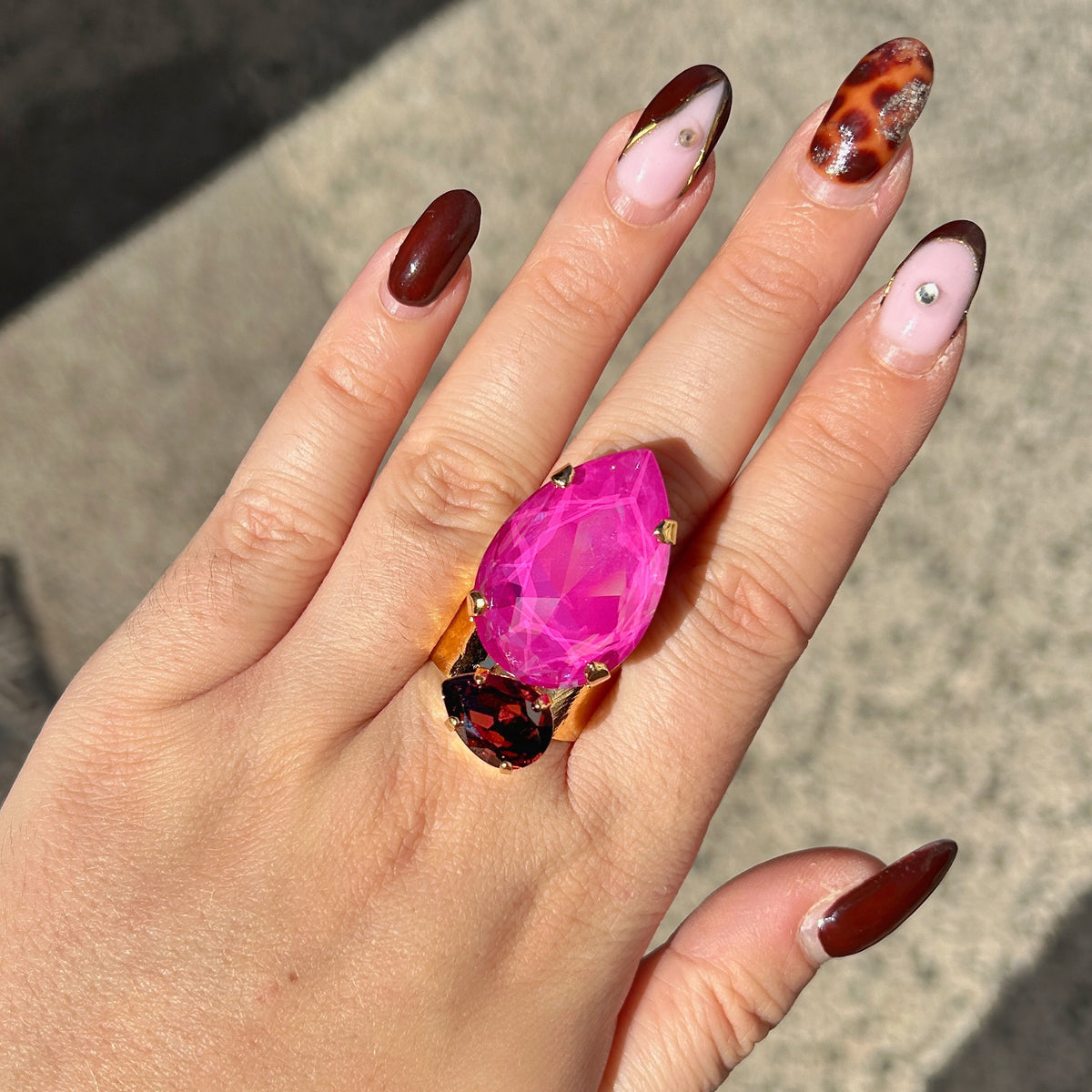 Bague Calypso Mûre Crézus avec grand cristal rose fuchsia en forme de goutte, petit cristal facetté couleur mûre et grenat, sertissage doré à griffes et anneau large martelé.