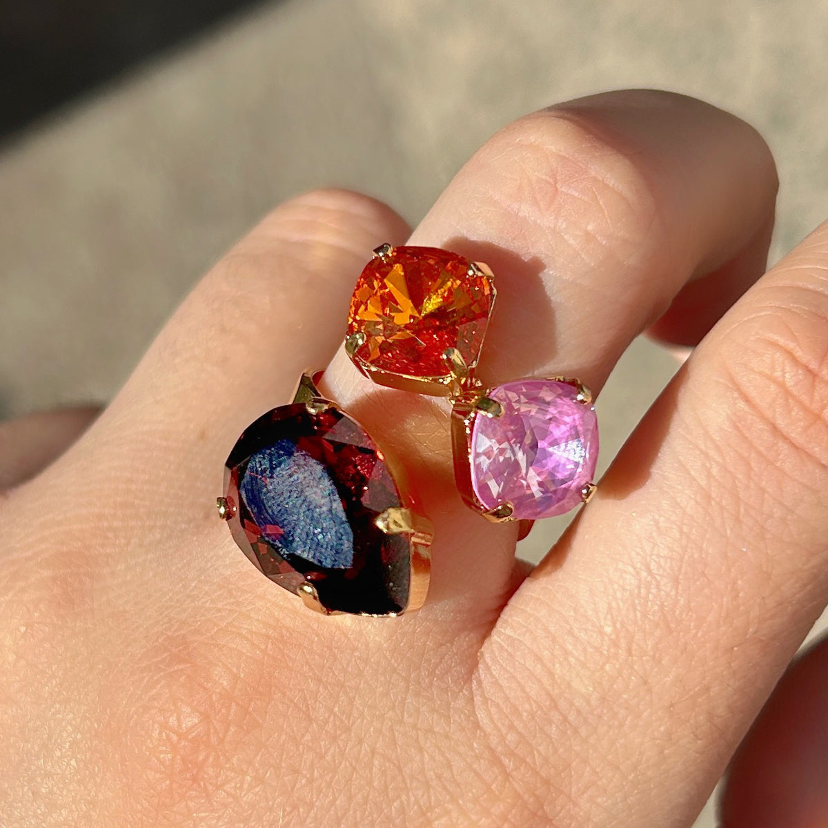 Bague Dalia Figue Crézus avec trois cristaux facettés couleur figue, orange et rose lilas, sertis sur une monture dorée asymétrique – Divinity Sète.