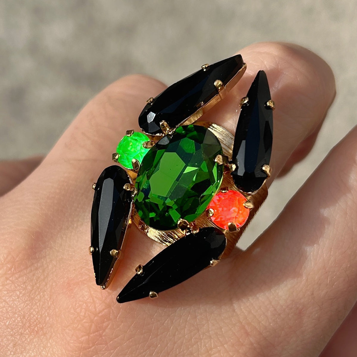 Bague réglable Lumen Fluo Crézus avec grand cristal ovale vert émeraude, quatre cristaux noirs allongés, cristaux vert fluo et orange sur monture dorée texturée.