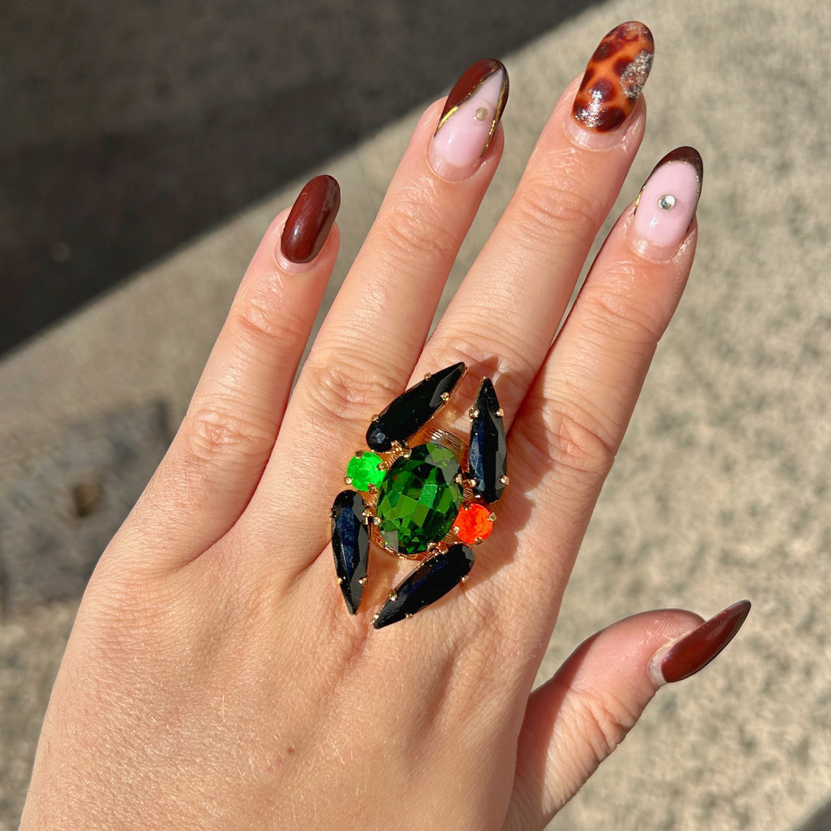 Bague réglable Lumen Fluo Crézus avec grand cristal ovale vert émeraude, quatre cristaux noirs allongés, cristaux vert fluo et orange sur monture dorée texturée.