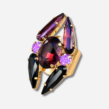 Bague réglable Lumen Mûre Crézus avec grand cristal ovale grenat, cristaux noirs et prune allongés, deux cristaux ronds violet orchidée et monture dorée texturée.