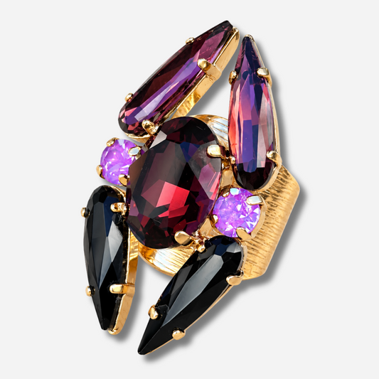 Bague réglable Lumen Mûre Crézus avec grand cristal ovale grenat, cristaux noirs et prune allongés, deux cristaux ronds violet orchidée et monture dorée texturée.