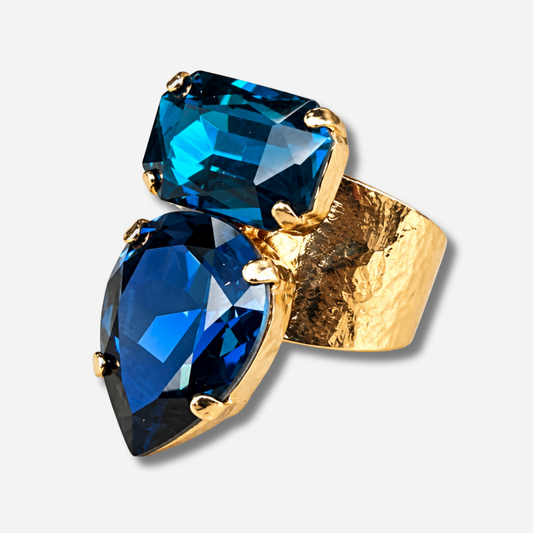 Bague Lyra Azur Crézus avec deux cristaux facettés bleu saphir et bleu pétrole, en forme de goutte et de rectangle, sur une large monture dorée texturée – Divinity Sète.