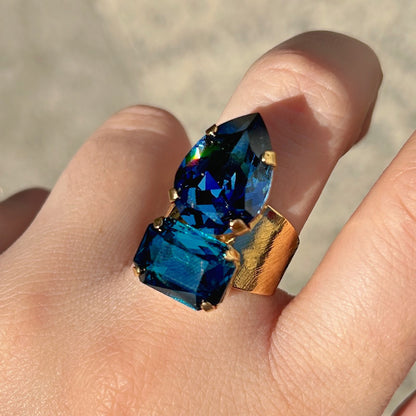 Bague Lyra Azur Crézus avec deux cristaux facettés bleu saphir et bleu pétrole, en forme de goutte et de rectangle, sur une large monture dorée texturée – Divinity Sète.