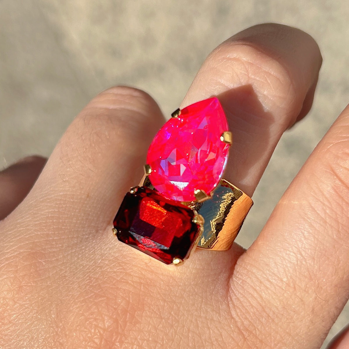 Bague Lyra Cerise Crézus avec cristal rose cerise en forme de goutte et cristal rectangulaire rouge rubis, sertis sur une large monture dorée texturée – Divinity Sète.