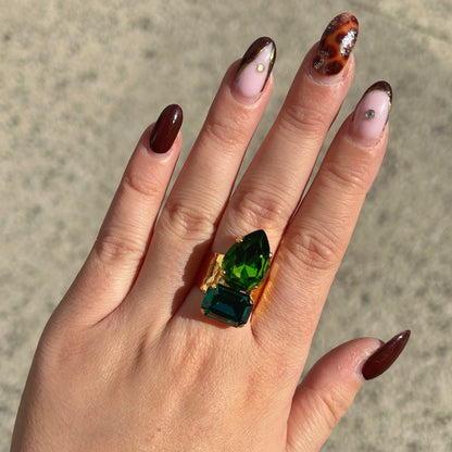 Bague Lyra Émeraude Crézus avec deux cristaux facettés vert émeraude et vert profond, en forme de goutte et de rectangle, sur une large monture dorée texturée – Divinity Sète.