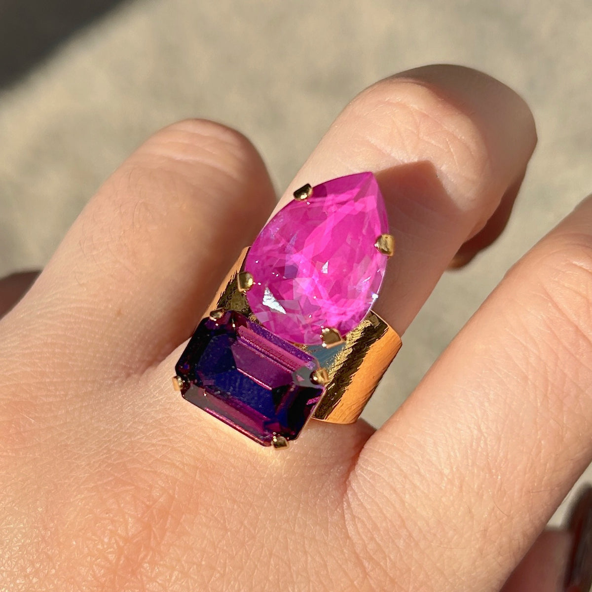 Bague Lyra Mûre Crézus avec cristal rose orchidée en forme de goutte et cristal rectangulaire violet mûre, sertis sur une large monture dorée texturée – Divinity Sète.