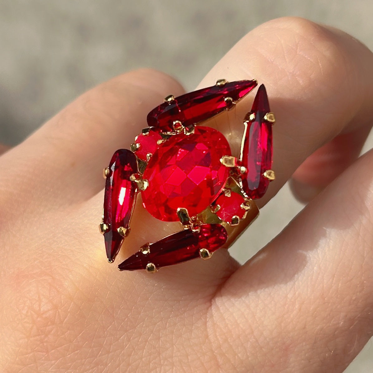 Bague Mira Cerise Crézus avec grand cristal ovale rouge cerise, quatre cristaux allongés rouge grenat, deux petits cristaux ronds rose cerise et monture dorée à anneau large.