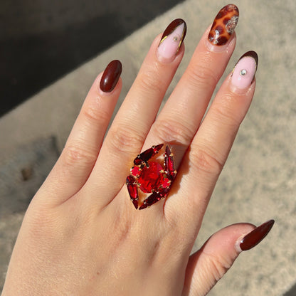 Bague Mira Cerise Crézus avec grand cristal ovale rouge cerise, quatre cristaux allongés rouge grenat, deux petits cristaux ronds rose cerise et monture dorée à anneau large.