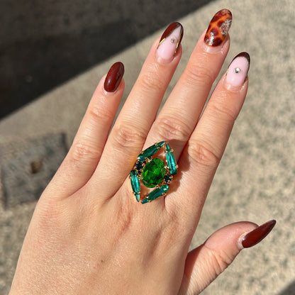 Bague Mira Émeraude Crézus avec grand cristal ovale vert émeraude, quatre cristaux allongés turquoise, petits cristaux vert canard et monture dorée à anneau large.