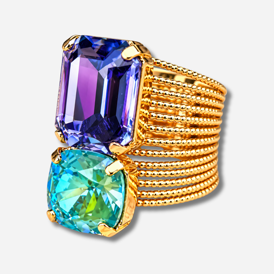 Bague Velora Blue Crézus dorée à large anneau composé de rangées perlées, ornée de deux grands cristaux facettés bleu violet et turquoise vert sertis de griffes dorées.