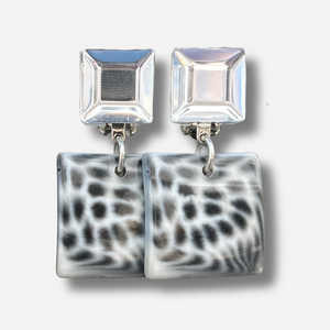 Boucles Albertine Blanc Francine Bramli Paris avec puce carrée argentée miroir et pendentif carré noir et blanc motif animalier, portées sur mannequin chez Divinity Sète.