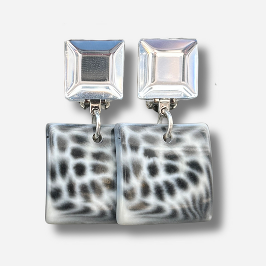 Boucles Albertine Blanc Francine Bramli Paris avec puce carrée argentée miroir et pendentif carré noir et blanc motif animalier, portées sur mannequin chez Divinity Sète.