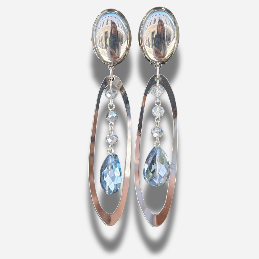 Boucles Cristol Silver Francine Bramli Paris en métal argenté avec cristaux facettés transparents et bleu glacier suspendus dans une monture ovale.