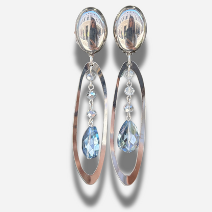 Boucles Cristol Silver Francine Bramli Paris en métal argenté avec cristaux facettés transparents et bleu glacier suspendus dans une monture ovale.