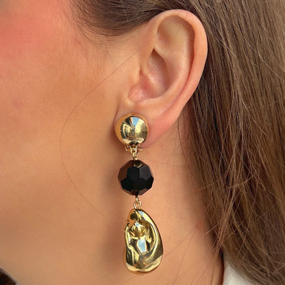 Boucles d'oreilles à clips Anastatia Noir Gold Francine Bramli Paris avec bouton rond doré effet miroir, perle noire facettée et pendentif goutte sculptural doré brillant – Divinity Sète.
