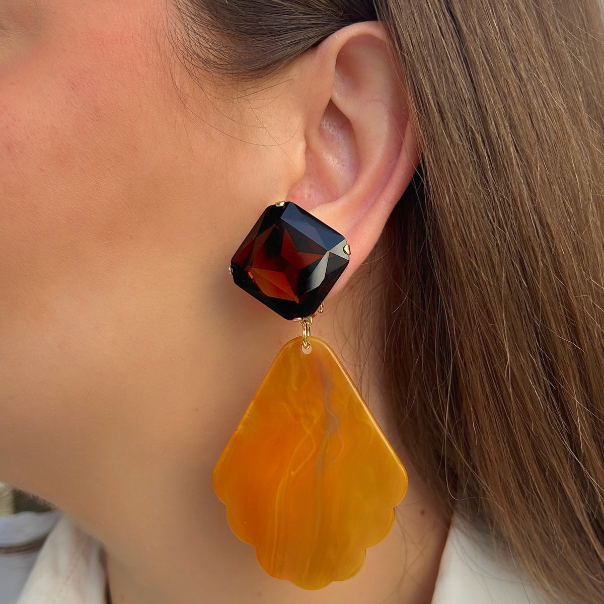 Boucles d’oreilles Aria à clips Francine Bramli Paris avec cabochons carrés facettés brun ambré et grands pendentifs orange marbré aux contours festonnés.