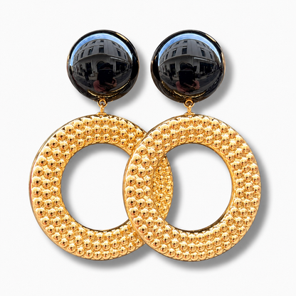 Boucles d’oreilles Avena Gold à clips Francine Bramli Paris, cabochons ronds noirs brillants et grands anneaux circulaires dorés ornés de petites perles en relief.