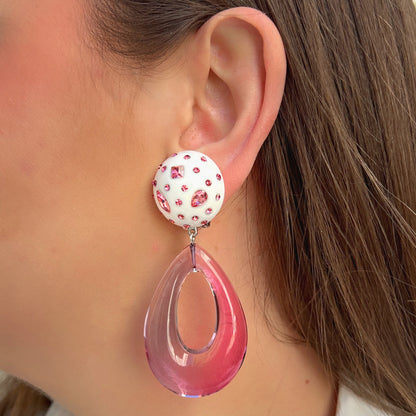 Boucles d'oreilles à clips Céleste Rose Francine Bramli Paris, attaches rondes blanches ornées de strass roses et pendentifs gouttes ajourées en résine rose translucide – Divinity Sète.