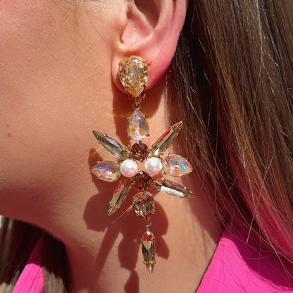 Boucles d'oreilles Celyna Gold à clips Crézus, modèle floral doré composé de cristaux facettés champagne et rose irisé en forme de goutte et de navette, avec perles blanches centrales et pampilles pendantes.