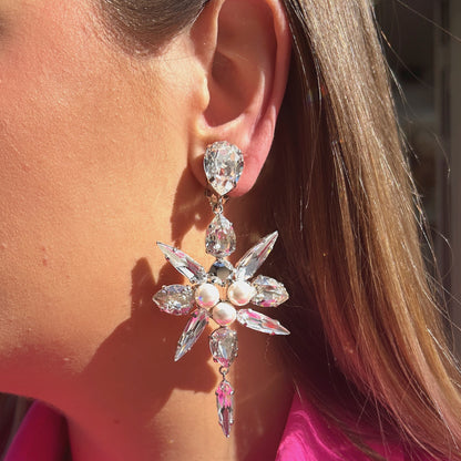 Boucles d'oreilles Celyna Silver à clips Crézus, modèle floral argenté composé de cristaux transparents facettés en forme de goutte et de navette, de trois perles blanches centrales et d'une pampille en cristal suspendue.