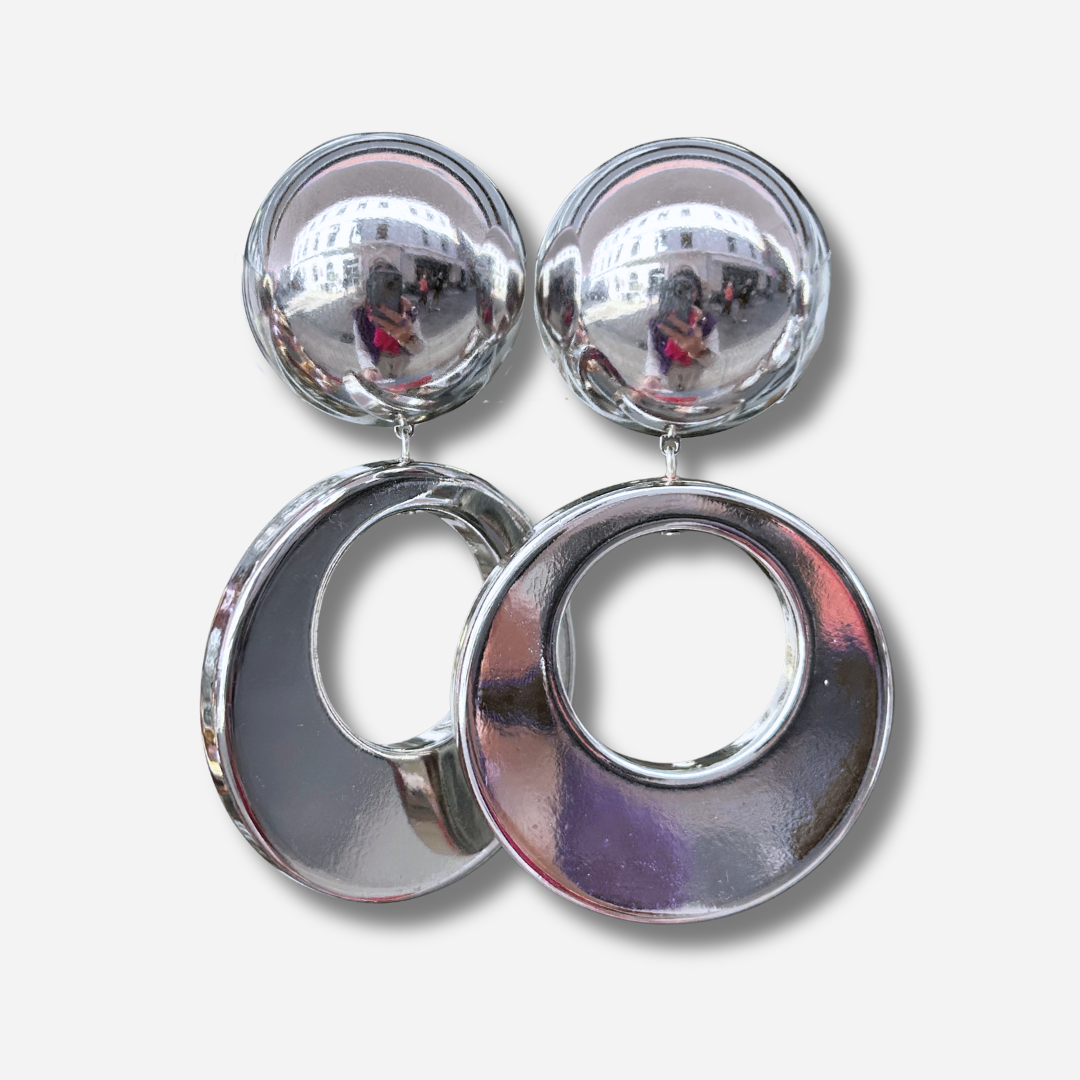 Boucles d'oreilles à clips Cloe Silver Francine Bramli Paris en résine argentée effet miroir, composées d'un gros bouton rond bombé et d'un large pendentif circulaire ajouré à finition métallisée brillante – Divinity Sète.