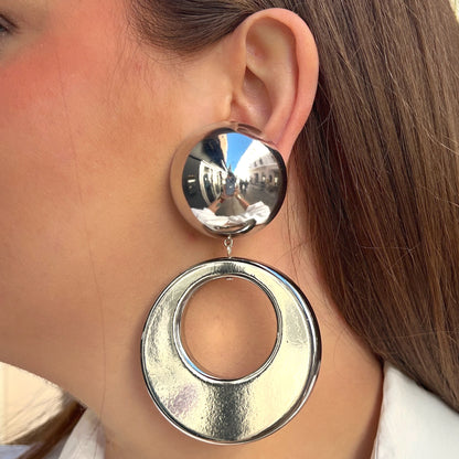 Boucles d'oreilles à clips Cloe Silver Francine Bramli Paris en résine argentée effet miroir, composées d'un gros bouton rond bombé et d'un large pendentif circulaire ajouré à finition métallisée brillante – Divinity Sète.