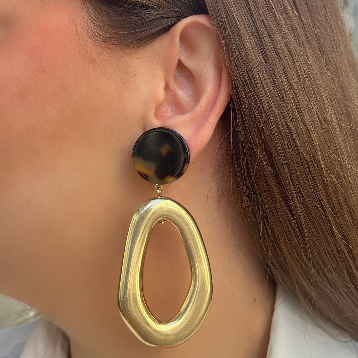 Boucles d’oreilles Lison Gold à clips Francine Bramli Paris, cabochons ronds effet écaille noir et ambre avec grands pendentifs ovales ajourés dorés brillants.