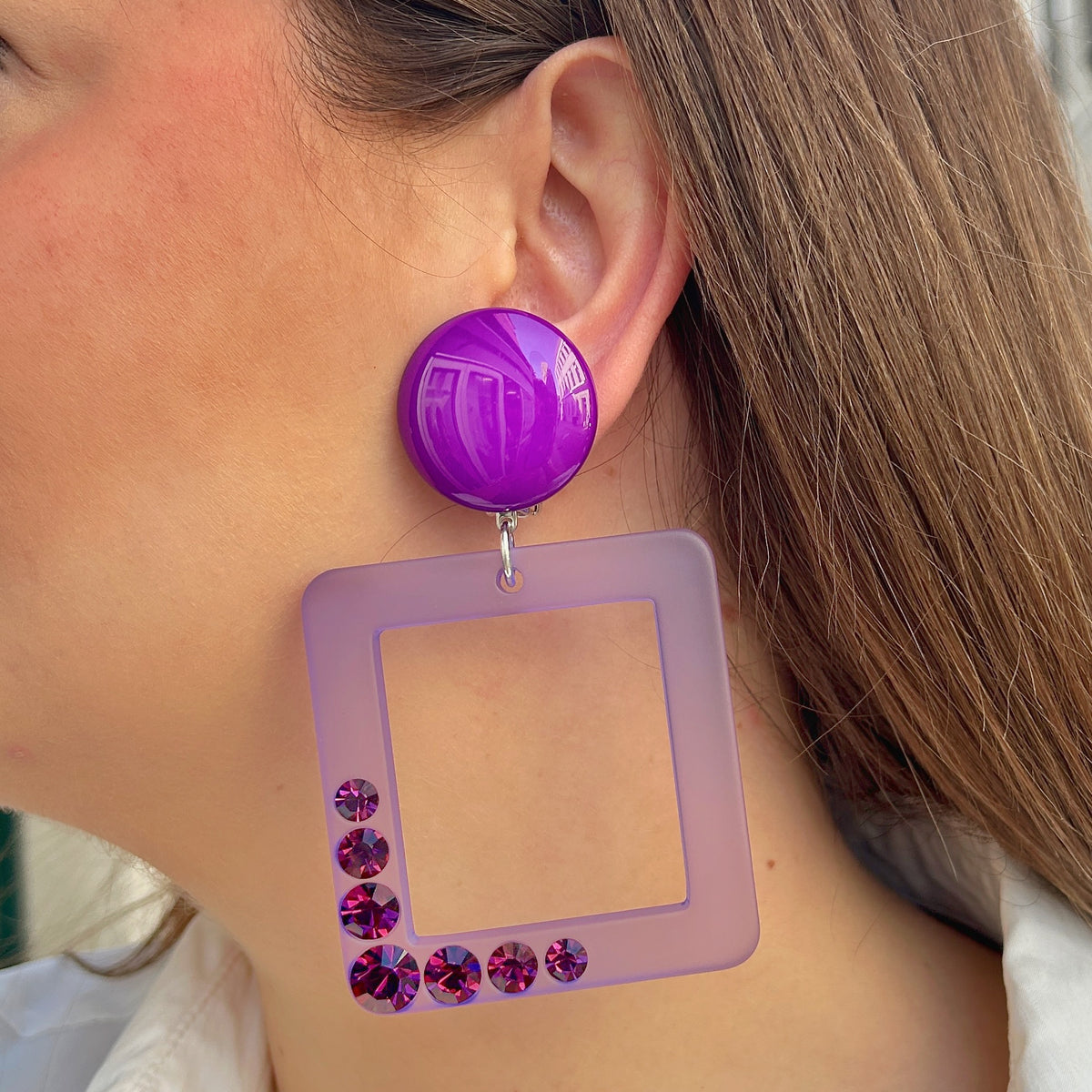 Boucles d’oreilles à clips Madison XL Violet Francine Bramli Paris, cabochons ronds violet brillant et grands pendentifs carrés ajourés lilas translucide ornés de cristaux violets scintillants.