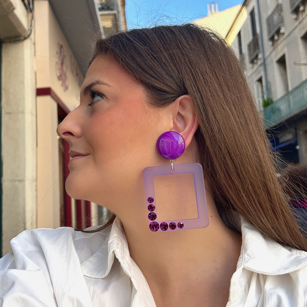 Boucles d’oreilles à clips Madison XL Violet Francine Bramli Paris, cabochons ronds violet brillant et grands pendentifs carrés ajourés lilas translucide ornés de cristaux violets scintillants.