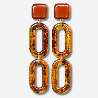 Boucles d’oreilles Noelia Ambre à clips Francine Bramli Paris, cabochons carrés marron translucide et doubles maillons ovales ajourés en résine effet écaille ambrée.