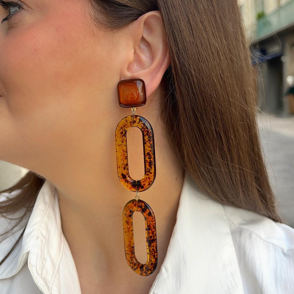 Boucles d’oreilles Noelia Ambre à clips Francine Bramli Paris, cabochons carrés marron translucide et doubles maillons ovales ajourés en résine effet écaille ambrée.