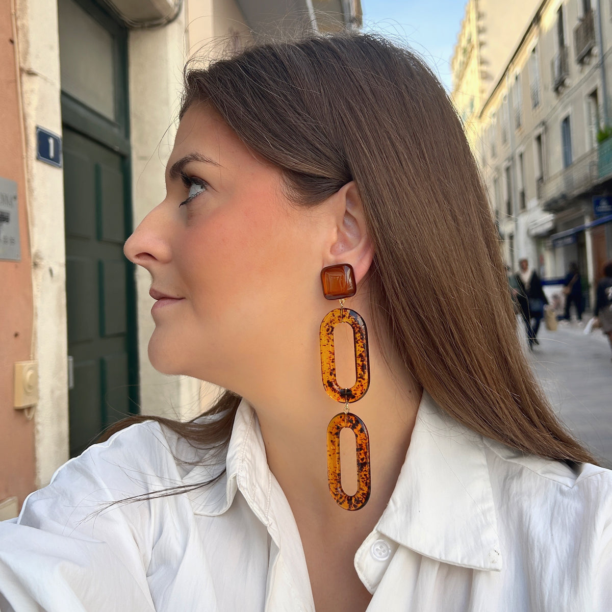 Boucles d’oreilles Noelia Ambre à clips Francine Bramli Paris, cabochons carrés marron translucide et doubles maillons ovales ajourés en résine effet écaille ambrée.