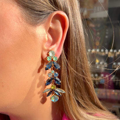 Boucles d’oreilles pendantes Ophéa Blue Crézus, monture dorée ornée de cristaux facettés bleu saphir, bleu ciel, turquoise et vert lime, disposés en cascade avec pierres rondes et marquises.