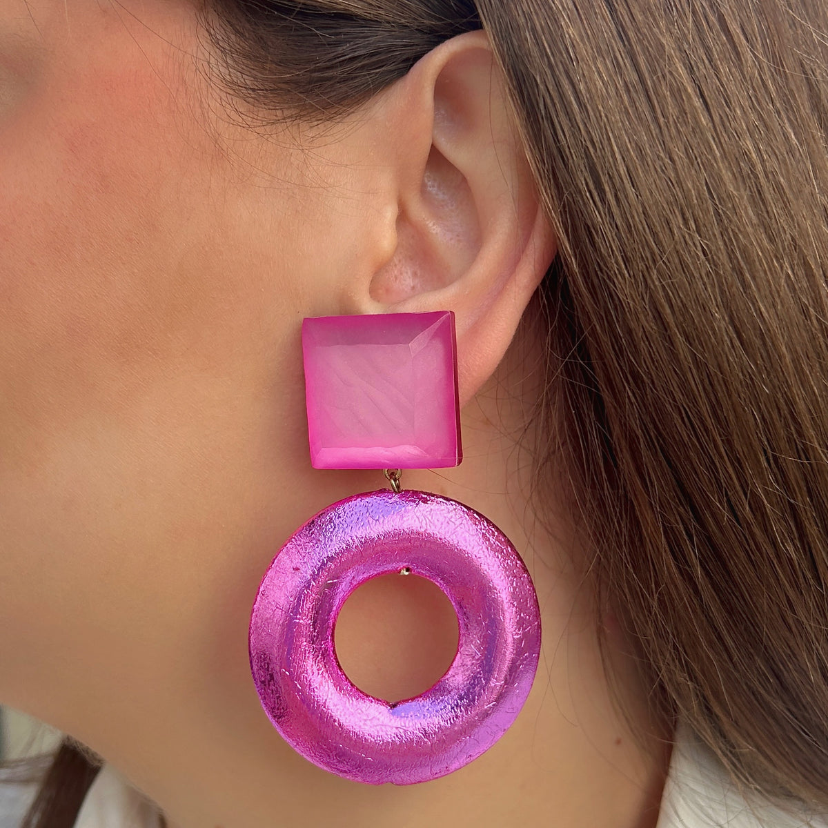 Boucles d’oreilles Rétro Rose Francine Bramli Paris portées avec une chemise blanche, modèle à clips avec cabochon carré rose et pendentif circulaire fuchsia brillant.