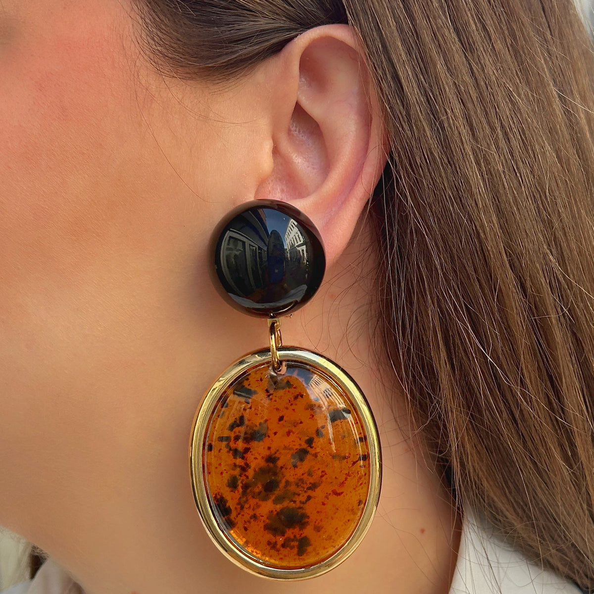 Boucles d’oreilles Tortuga Ambre à clips Francine Bramli Paris, cabochons ronds brun foncé et grands pendentifs ovales ambre orangé moucheté de brun avec contour doré.