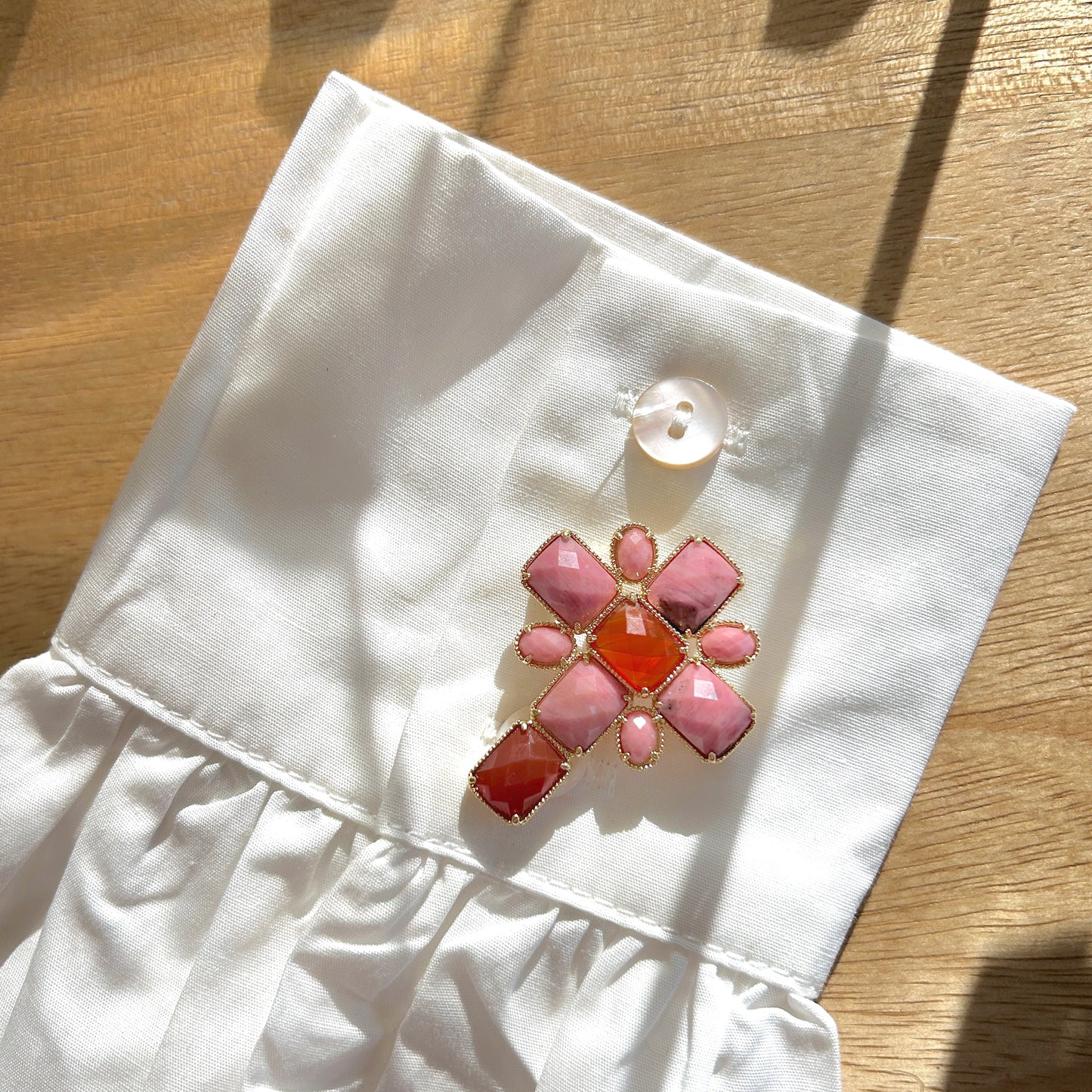 Détail de la broche croix rose pierres facettées et monture dorée
