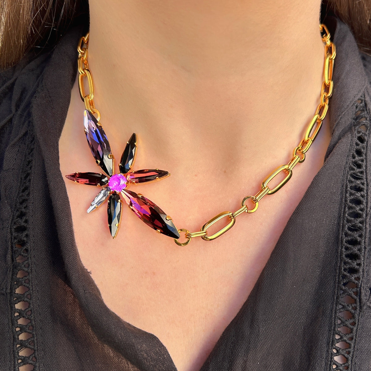 Collier Capella Mûre Crézus avec chaîne dorée à larges maillons et fleur asymétrique en cristaux facettés violets, roses, noirs et transparents.